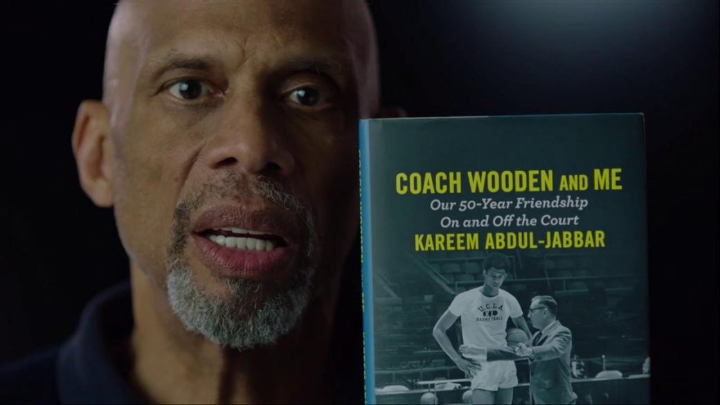 A man holding up a book with the title of coach wooden and his name.