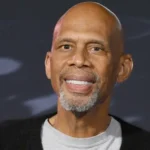 A bald man with white teeth and black jacket.