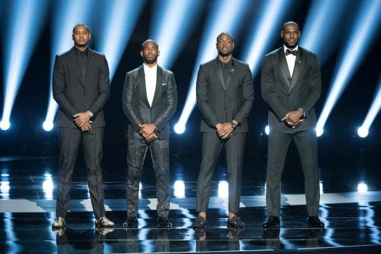 Four men in suits stand on a stage.