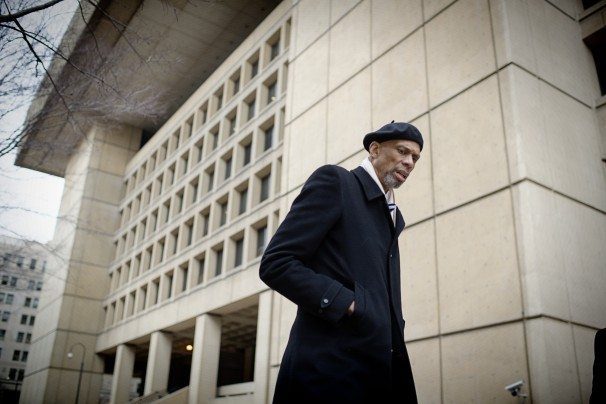 A man in a hat and coat walking outside of a building.