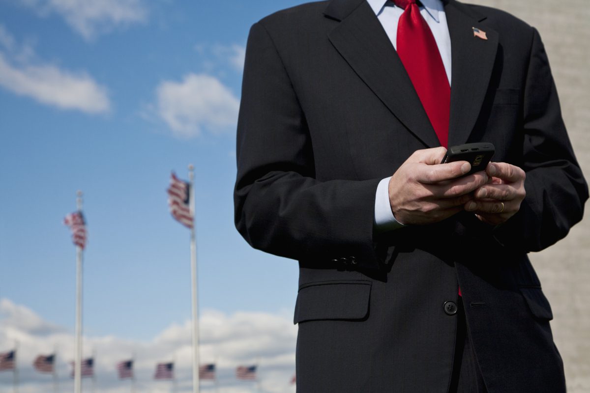 A man in suit and red tie holding a cell phone.