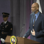 A man in suit and tie standing at a podium.