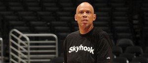 A bald man in black shirt standing on basketball court.