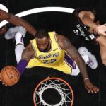 A basketball player in the air with his feet on the rim.