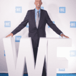 A man in suit and tie standing behind large letters that spell out " we ".