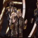 A group of people standing on stage with one man clapping.