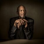 Kareem Abdul Jabbar sitting at a table with his hands crossed.