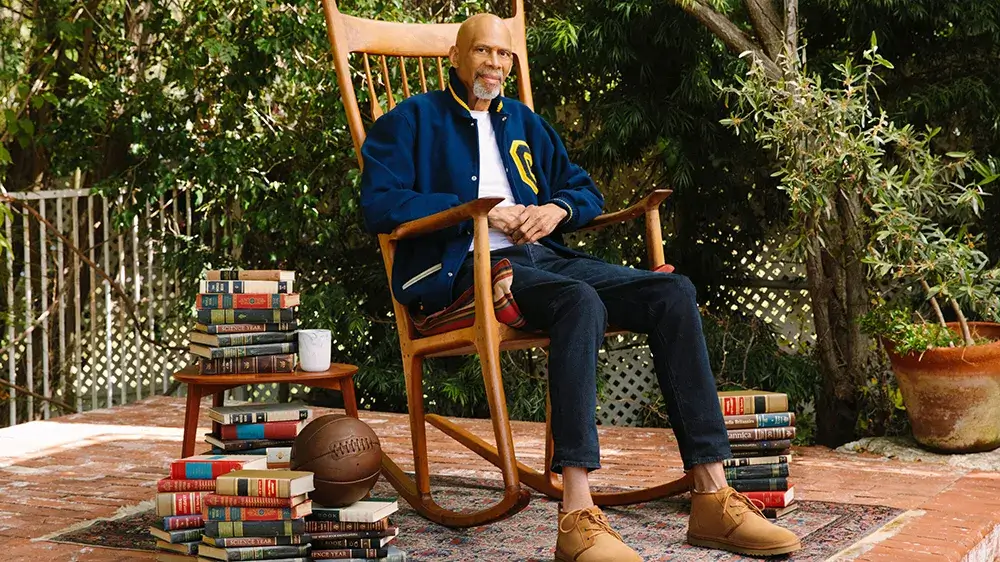 Kareem Abdul Jabbar sitting in a rocking chair with books around him.
